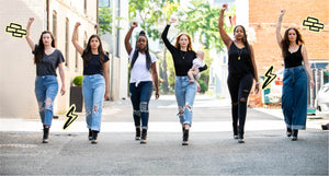 Image of six women wearing shirts and jeans walking in a row. They are wearing VOTE boots and raising their right fists in the air.