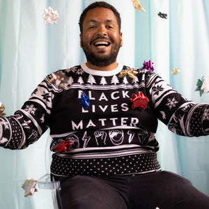 A person wearing the Black Lives Matter Holiday Sweater. There is an ice blue background and bows around them.