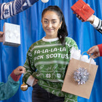 Load image into Gallery viewer, Photo of a person wearing the Fa-La-La-La F*ck SCOTUS Holiday Sweater. There are hands holing gifts around them and a blue background.