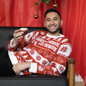 A person wearing the We Want Change Holiday Sweater, they are laying on a couch holding a pastry.. There is a red background.