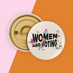 Load image into Gallery viewer, Image of cream colored safety pin style button with black design reading "Women Are Voting" with various inclusive feminine figures