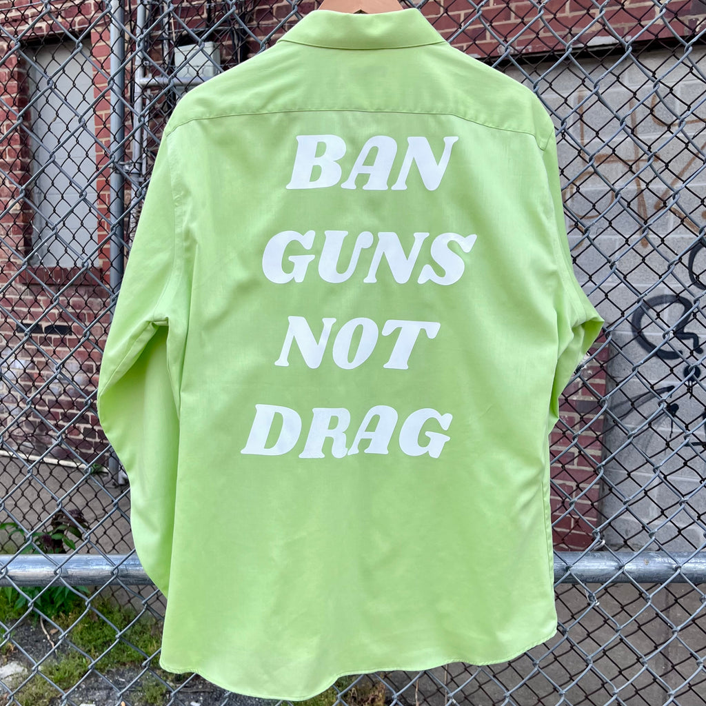 Green upcycled button down with "Ban Guns Not Drag" printed across the back in a 70s font.