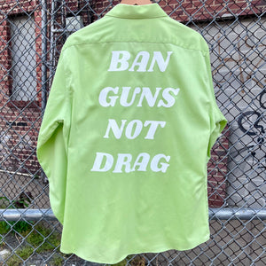 Green upcycled button down with "Ban Guns Not Drag" printed across the back in a 70s font.
