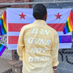 Load image into Gallery viewer, Woman in front of rainbow flags wears a yellow upcycled button down with &quot;Ban Guns Not Drag&quot; printed across the back in a 70s font.
