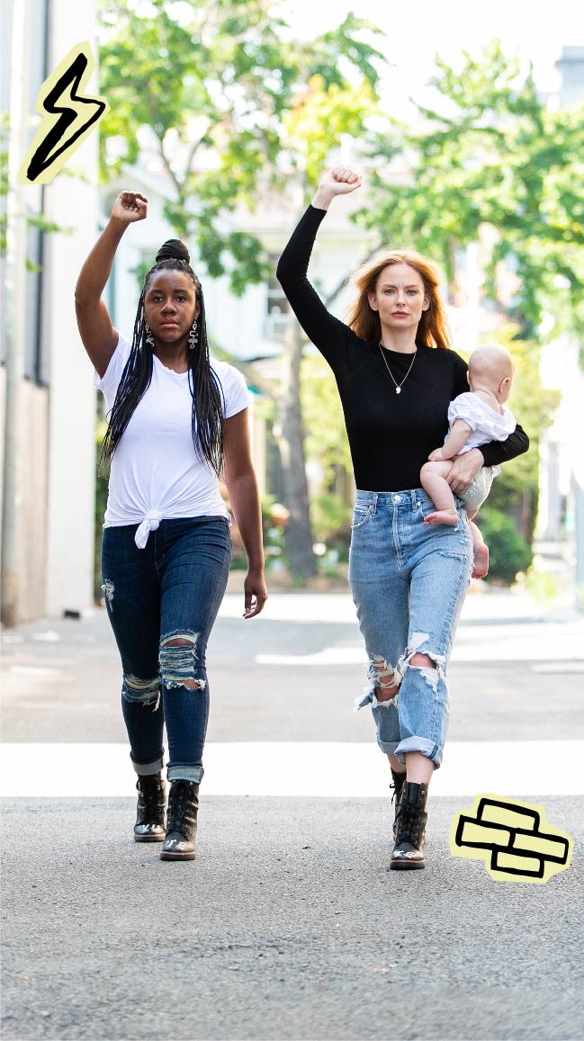 Image of two women wearing shirts and jeans with VOTE boots. They are both raising their right fists in the air.