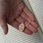 Load image into Gallery viewer, &quot;Human Rights are Women&#39;s rights&quot; HRC quote bronze medallion necklace sitting in a hand above a book 
