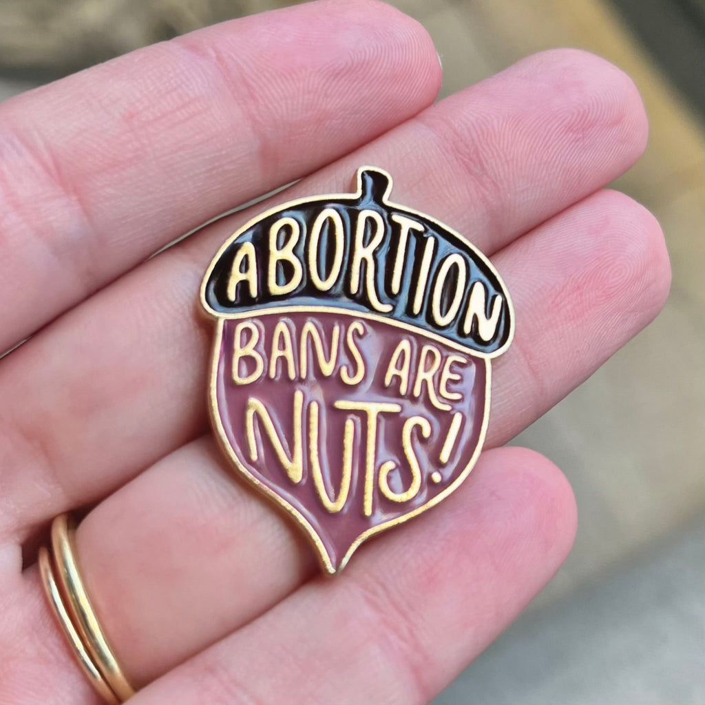 Acorn shaped enamel pin with "abortion bans are nuts" design