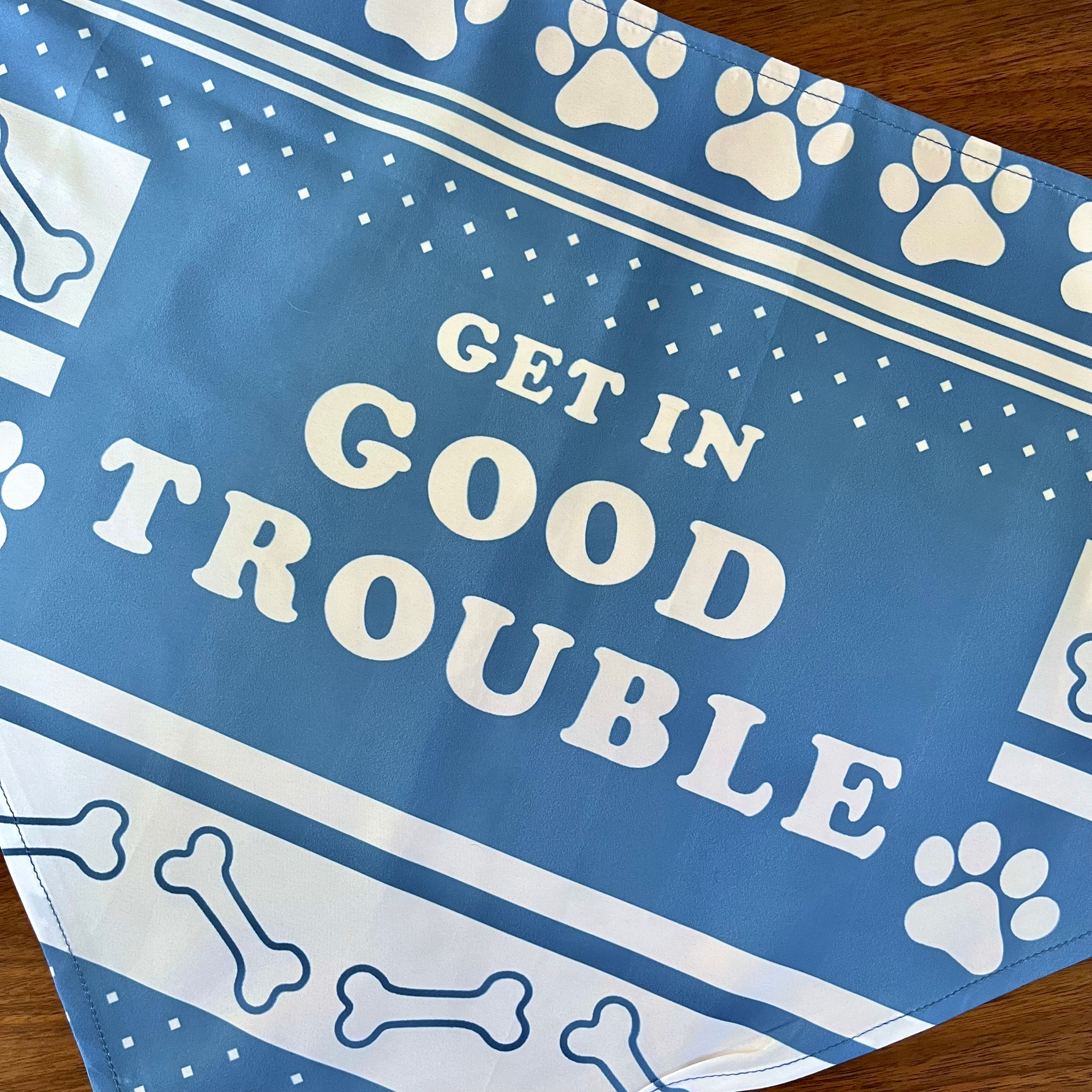 Flat lay close up of blue Dog Bandana with "Get In Good Trouble" design with pay prints and bones