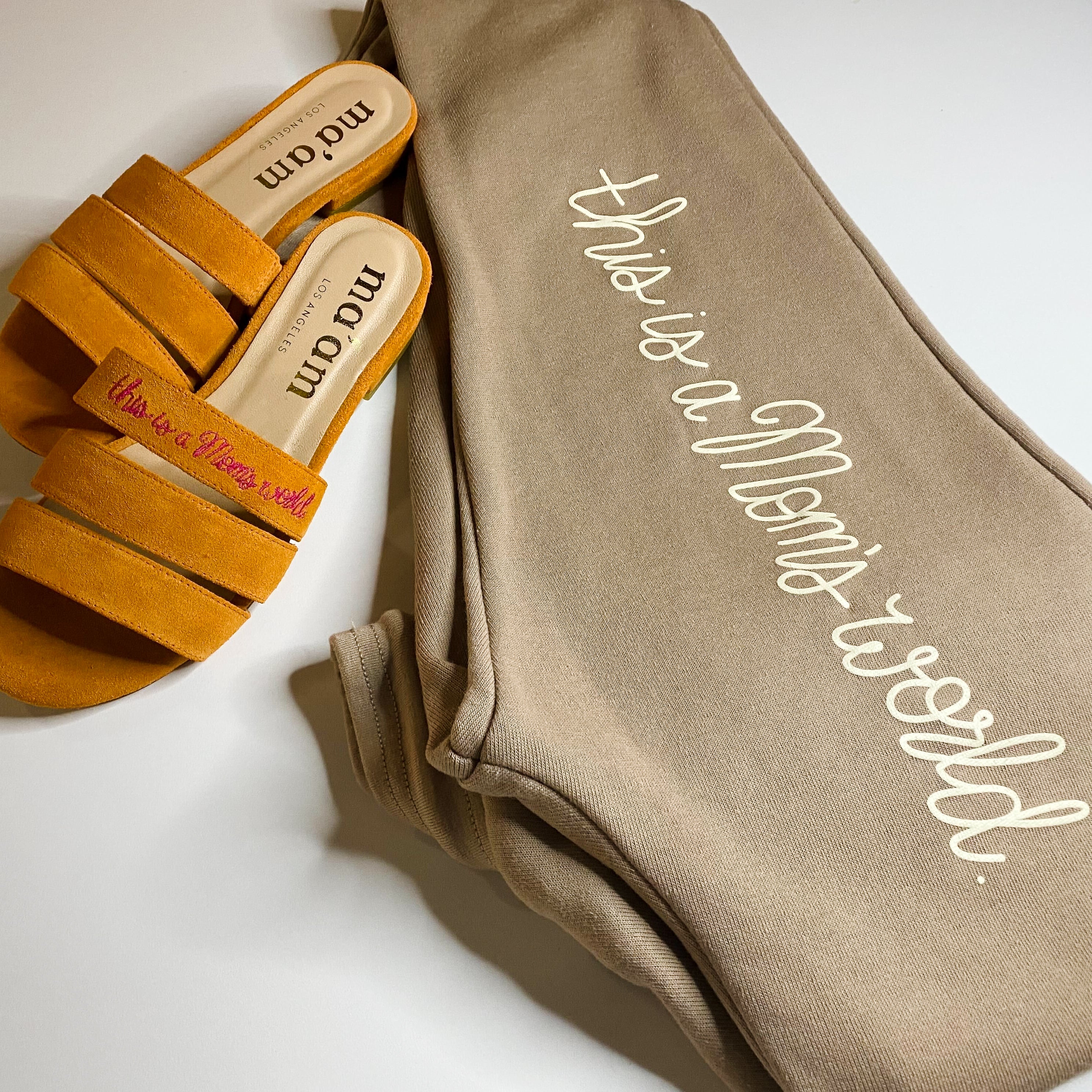 Image of Flat lay of Ma'am Shoes "This Is A Mom's World" joggers and slides. | The Outrage