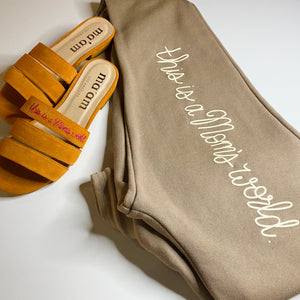 Image of Flat lay of Ma'am Shoes "This Is A Mom's World" joggers and slides. | The Outrage