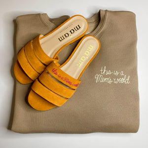 Image of Flat lay of Ma'am Shoes "This Is A Mom's World" sweatshirt and slides. | The Outrage	
