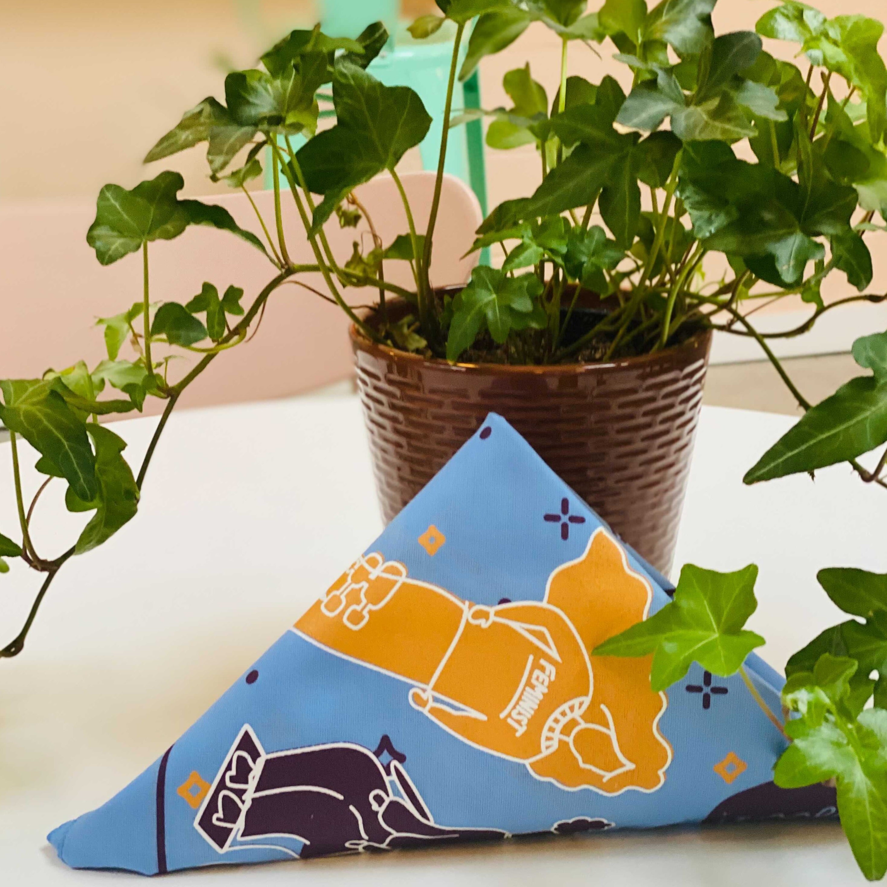 The Outrage's Accessibility for All bandana in blue folded on a table next to a plant.