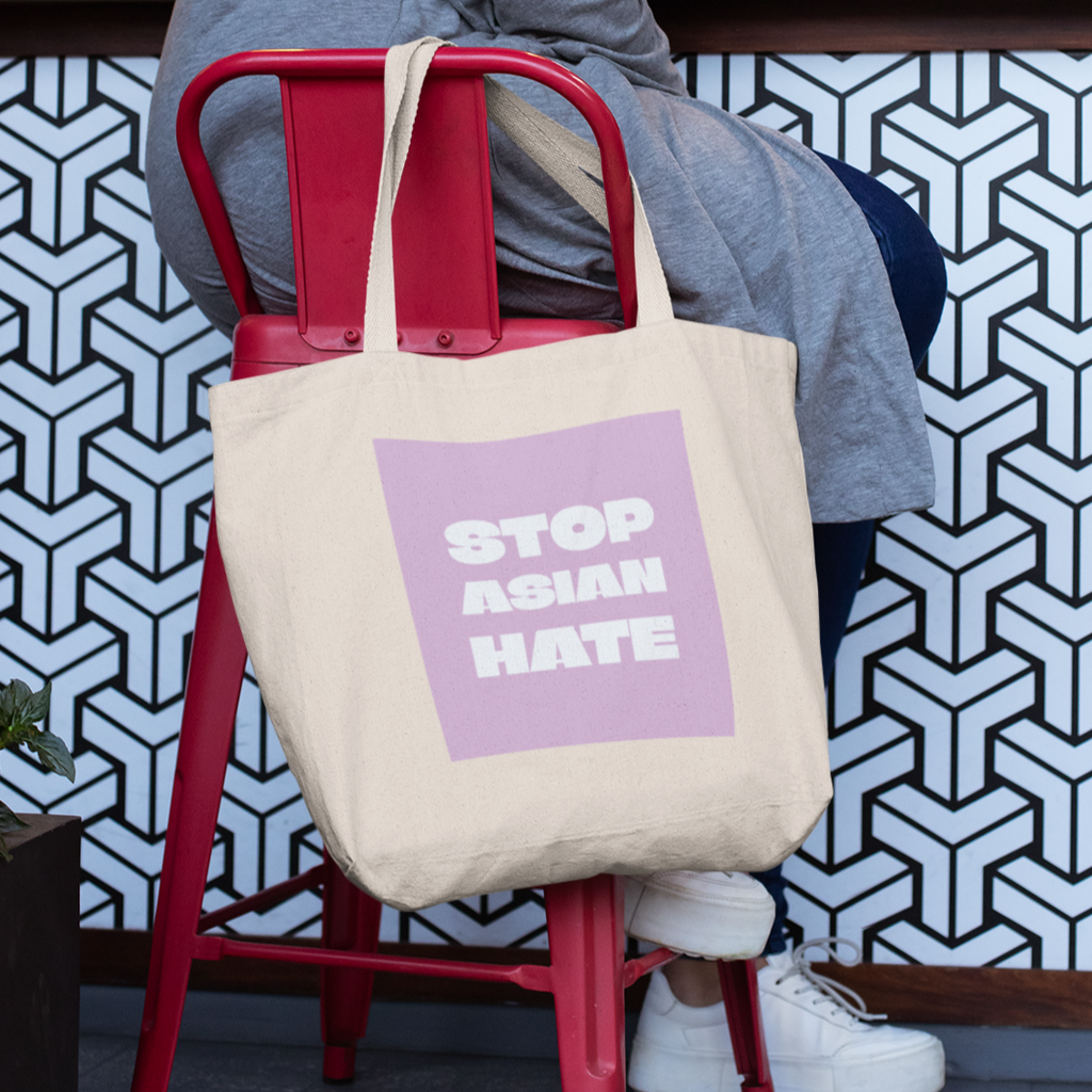 Stop Asian Hate tote bag on chair with person sitting.