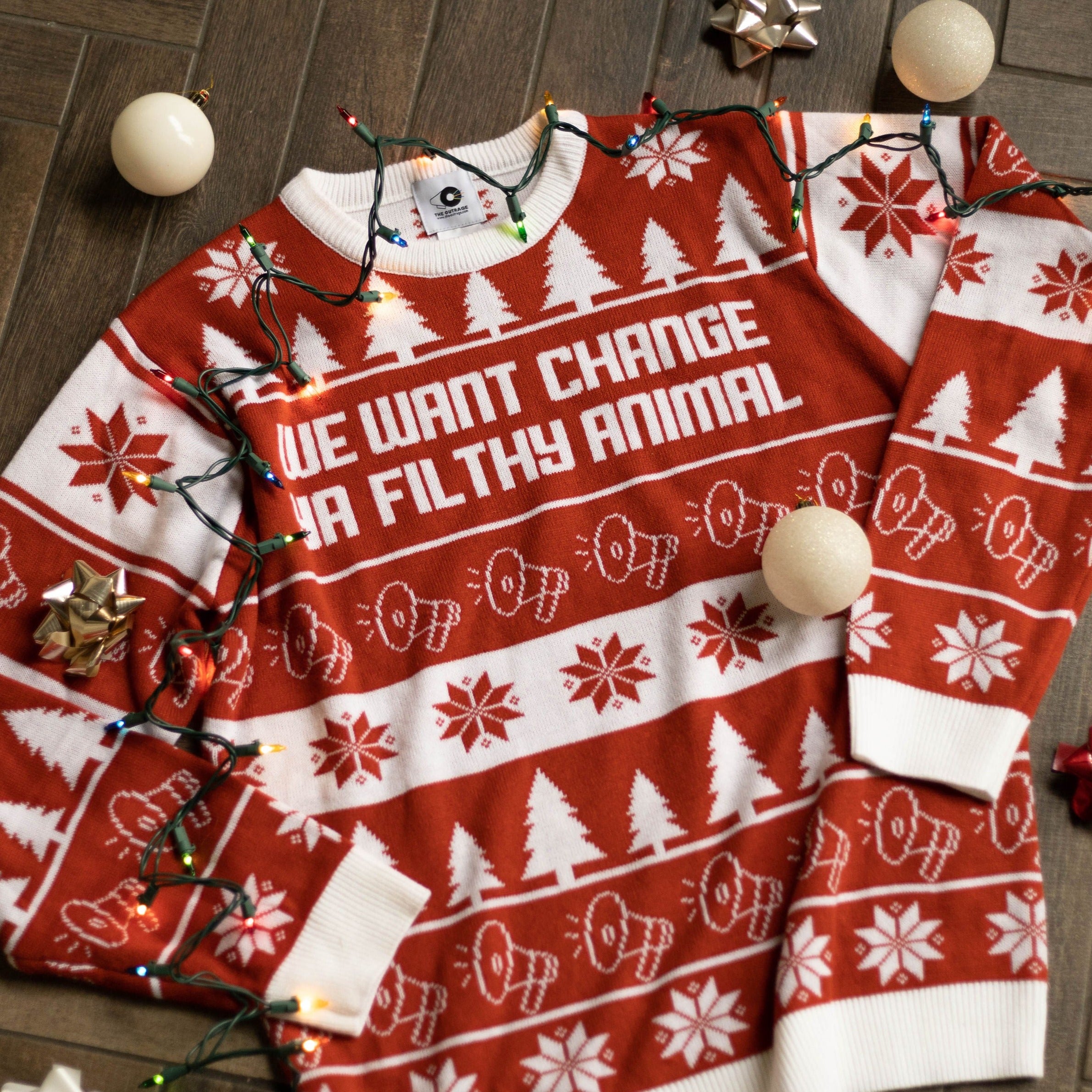 A flat lay of the We Want Change Holiday Sweater. There are colorful holiday lights, ornaments, and bows around it.