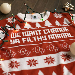 A flat lay of the We Want Change Holiday Sweater. There are colorful holiday lights, ornaments, and bows around it.