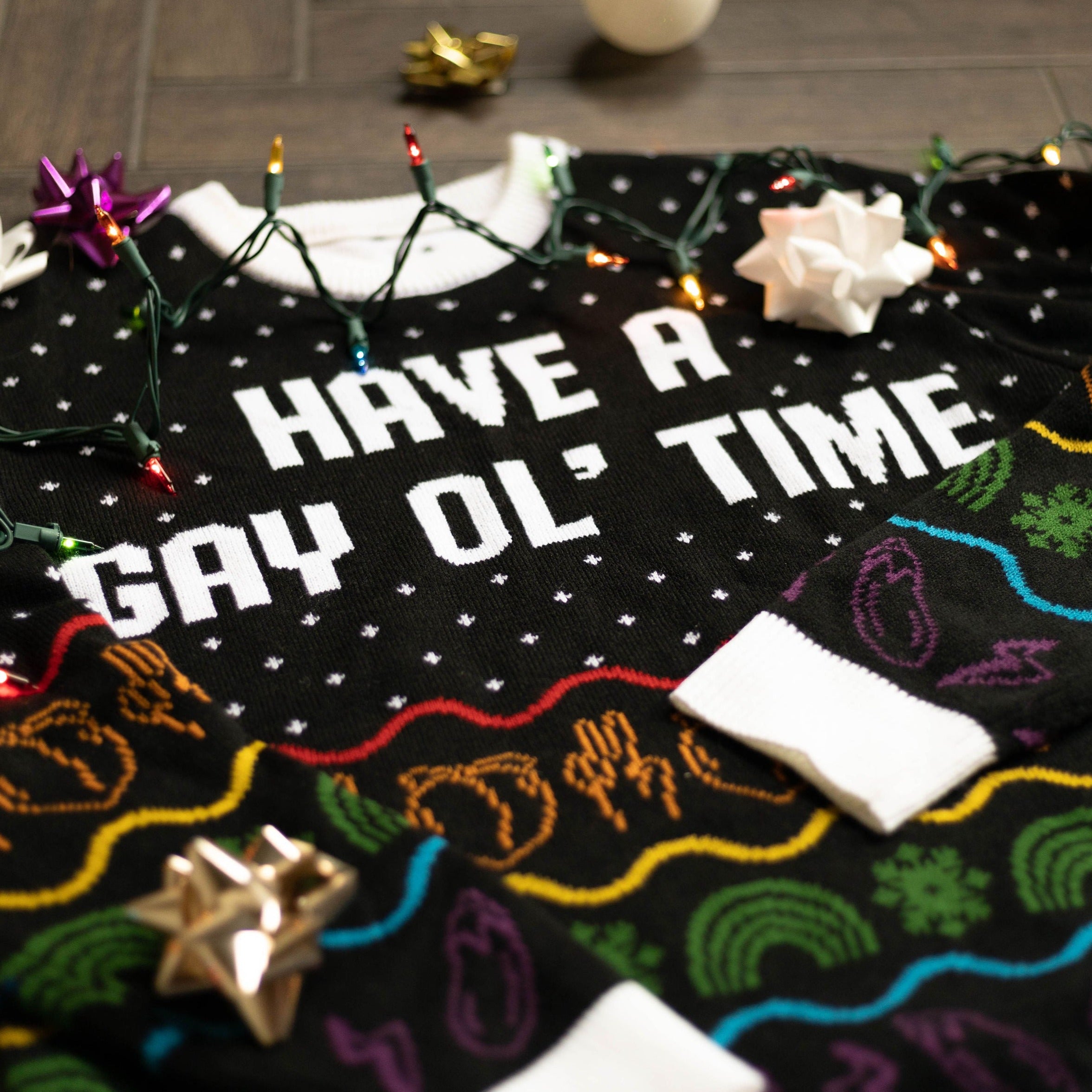 A flat lay of the Have A Gay Ol' Time Holiday Sweater. There are colorful holiday lights, bows, and ornaments around it.