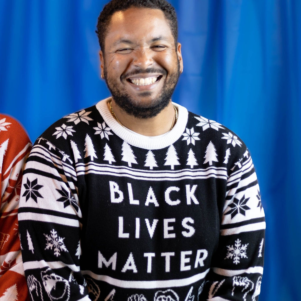 A person wearing the Black Lives Matter Holiday Sweater. There is a blue background.