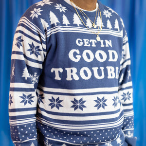 A person wearing the Get In Good Trouble Holiday Sweater. There is a blue background.
