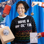 Load image into Gallery viewer, A person wearing the Have A Gay Ol&#39; Time Holiday Sweater. There are hands holding gifts around them and a blue background.
