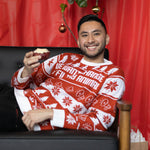 Load image into Gallery viewer, A person wearing the We Want Change Holiday Sweater, they are laying on a couch holding a pastry.. There is a red background.

