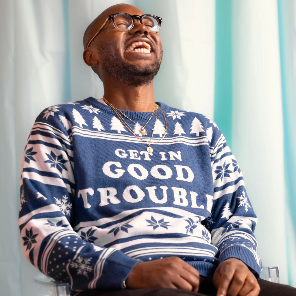 A person wearing the Get In Good Trouble Holiday Sweater. There is an ice blue background.