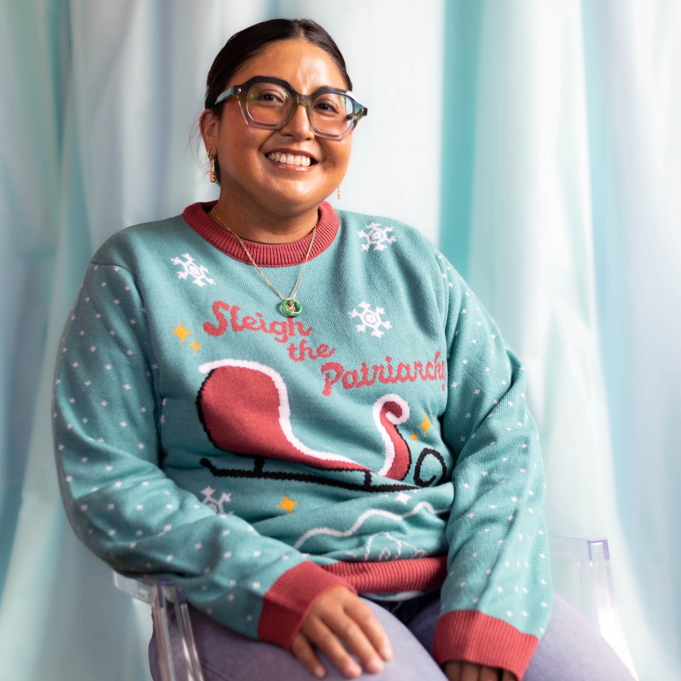 A person wearing the Sleigh The Patriarchy Holiday Sweater. There is an ice blue background.