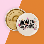 Load image into Gallery viewer, Image of cream colored safety pin style button with black design reading &quot;Women Are Voting&quot; with various inclusive feminine figures

