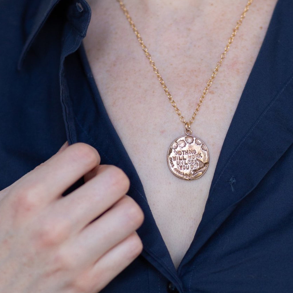"Nothing will work unless you do" Maya Angelou quote on a bronze medallion necklace worn by a woman in a navy button down