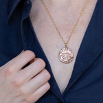 Load image into Gallery viewer, &quot;Nothing will work unless you do&quot; Maya Angelou quote on a bronze medallion necklace worn by a woman in a navy button down
