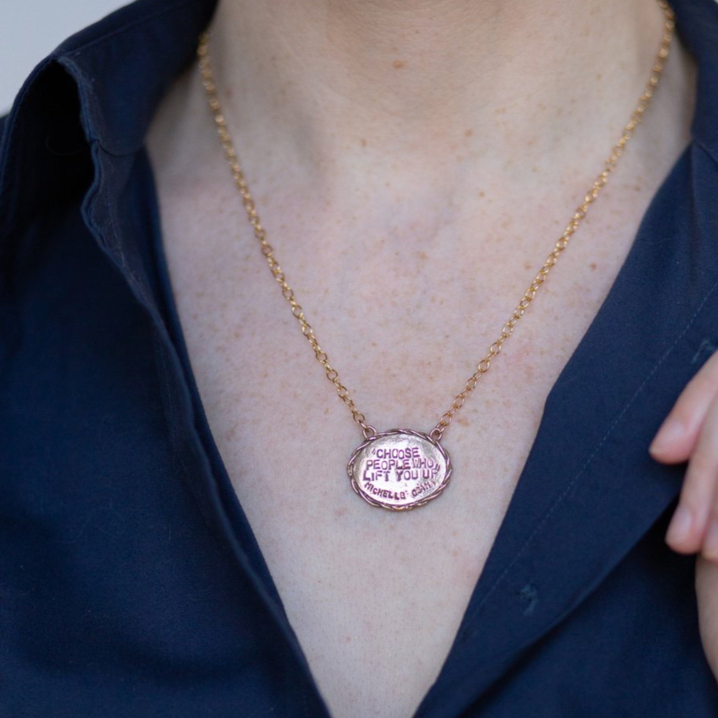 Bronze oval necklace on a woman in a navy button down "Choose People Who Lift You UP"