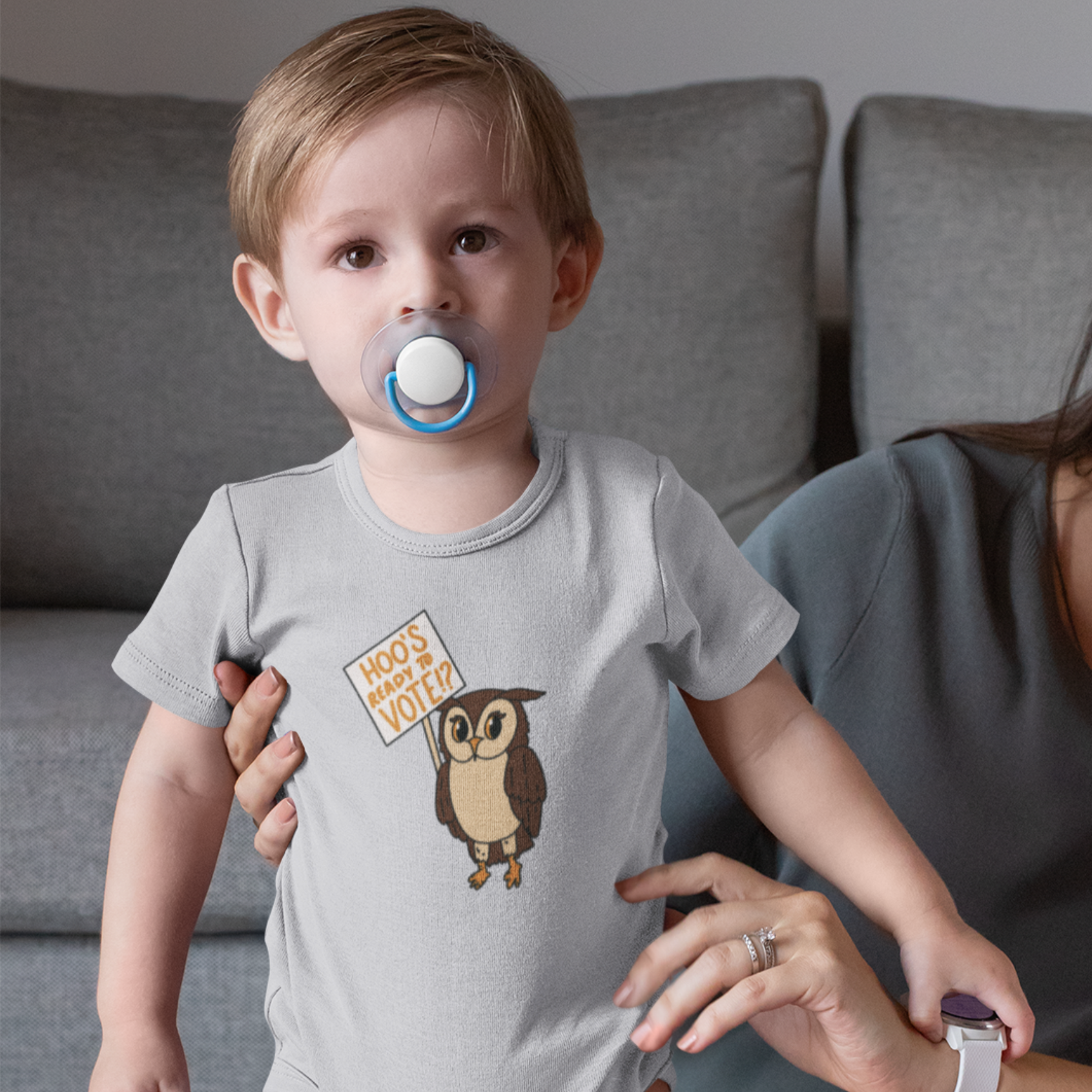 Toddler with a pacifier and heather grey onesie with "Hoo's Ready To Vote" owl design