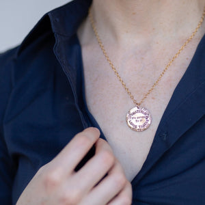 Woman in a blue shirt wearing a bronze necklace with a medallion with boot tracks reading "Whatever you choose to do Leave Tracks"