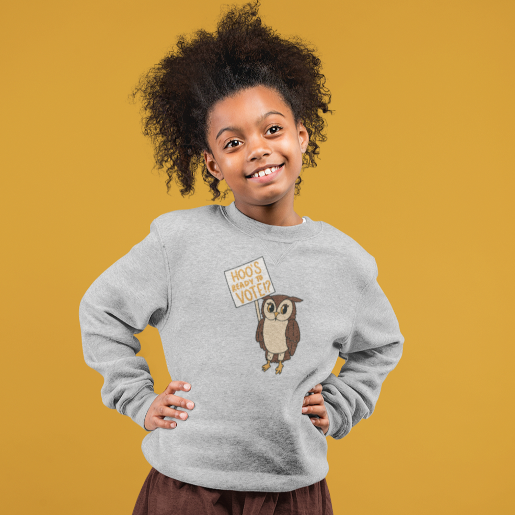 Girl with curly hair stands with her hands on her hips wearing a gray sweatshirt with "Hoo's ready to vote?" design 